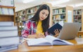 Female college student working on laptop and searching for books to study, make report, find useful information in college room. Royalty Free Stock Photo