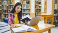 Female college student working on laptop and searching for books to study, make report, find useful information in college room. Royalty Free Stock Photo