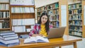 Female college student working on laptop and searching for books to study, make report, find useful information in college room. Royalty Free Stock Photo