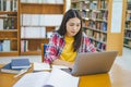 Female college student working on laptop and searching for books to study, make report, find useful information in college room. Royalty Free Stock Photo