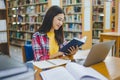 Female college student working on laptop and searching for books to study, make report, find useful information in college room. Royalty Free Stock Photo