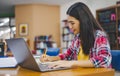 Female college student working on laptop and searching for books to study, make report, find useful information in college room. Royalty Free Stock Photo