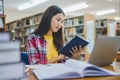 Female college student working on laptop and searching for books to study, make report, find useful information in college room. Royalty Free Stock Photo