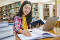 Female college student working on laptop and searching for books to study, make report, find useful information in college room. Royalty Free Stock Photo