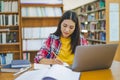 Female college student working on laptop and searching for books to study, make report, find useful information in college room. Royalty Free Stock Photo