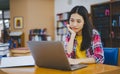 Female college student working on laptop and searching for books to study, make report, find useful information in college room. Royalty Free Stock Photo