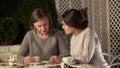 Female comforting upset sister, sitting outside on terrace and drinking coffee