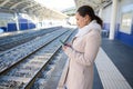 Female commuter using mobile phone while waiting high speed train at platform station, planning a route for railway stop Royalty Free Stock Photo