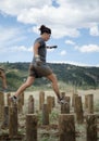 Female competitor running across tall wooden stumps