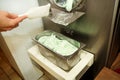 Female confectioner in chef uniform is working on ice cream maker machine. Producing mint ice cream flavors.