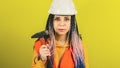 Female construction worker in overalls with hammer on yellow background in studio. Young woman in white hard hat holding Royalty Free Stock Photo