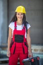 Female construction worker in overalls and a helmet holds a toolbox outdoors