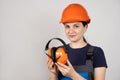 Female construction worker in protective helmet holding earmuffs on white background.