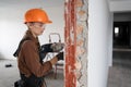 Female construction worker using hammer drill. Builder woman with pneumatic hammer drill perforator making hole in wall Royalty Free Stock Photo