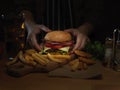 Female cook arranging fresh tasty gilled burger on wooden tray ready to serve with french fries