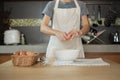 Female cook in a white apron is cracking an egg in home`s kitchen