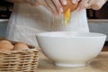 Female cook in a white apron is cracking an egg in home`s kitchen