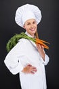 Female cook in white uniform with bunch of carrots