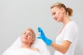 A female cosmetologist in rubber gloves shows a test tube to a client. A woman lying on a couch in defocus. Copy space