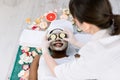 Female cosmetologist in uniform and protective gloves doing cucumber mask on eyes for relaxation in beauty salon