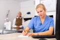 Female cosmetologist using computer while patient waiting