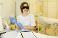 Female cosmetologist wearing special purpose glasses and latex gloves near permanent makeup device.