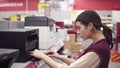Female costumer choosing new printer in electronics department in appliance store. Examining it carefuly. Looking for