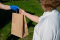 Female courier in gloves bringing food package to retired old woman. Woman handing a paper bag with groceries to a