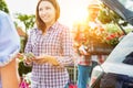 Female customer giving cash payment to the shop owner against mature gardener putting flowers on car trunk