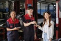 Female customer receives key from automotive workers after car repair at garage.
