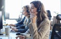 Female customer support operator with headset and smiling, with collegues at background