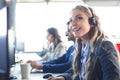 Female customer support operator with headset and smiling, with collegues at background