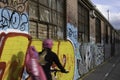 Cyclist (motion blur) wearing helmet cycles down a path along a wall with graffiti