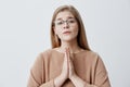 Female with dark eyes wearing eyeglasses having hopeful expression keeping her hands together asking for something Royalty Free Stock Photo