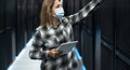 Female data center technician working inside server rack room while wearing facemask Royalty Free Stock Photo