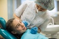 Female dentist doing teeth checkup of little girl looking with fear sitting in a dental chair