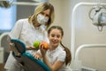 Female dentist gives apple for smiling teenage girl in modern clinic