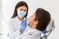 Female dentist in protective mask drilling male patient teeth Royalty Free Stock Photo