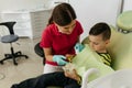 Female dentist teaching boy how to brush teeth in the dentists chair