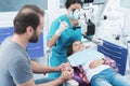 A female dentist is treating a girl. She is sitting on the dental chair. She is afraid and her father holds her hand. Royalty Free Stock Photo