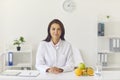 Female dietician sitting at office desk with fruit and measuring tape looking at camera