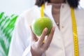 Female dietitian in apron and tape measure holding apple