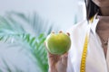 Female dietitian in apron and tape measure holding apple