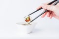 Female dipping tasty sushi makaki or uramaki with chopsticks into bowl with soy sauce on white background. Space for copy