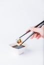 Female dipping tasty sushi makaki or uramaki with chopsticks into bowl with soy sauce on white background. Space for copy