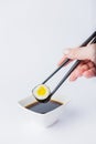 Female dipping tasty sushi makaki or uramaki with chopsticks into bowl with soy sauce on white background. Space for copy