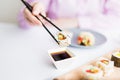 Female dipping tasty sushi roll with chopsticks into bowl with soy sauce at the table Royalty Free Stock Photo