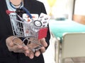 Female Doctor with black suit is holding small shopping cart With colorful pills , injection syringe and stethoscope.