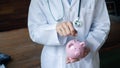 Female doctor is deposit coins into the pink piggy bank, saving protection concept Royalty Free Stock Photo