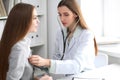 Female doctor examining her patient with stethoscope while sitting at the table near the window in hospital. Physician Royalty Free Stock Photo